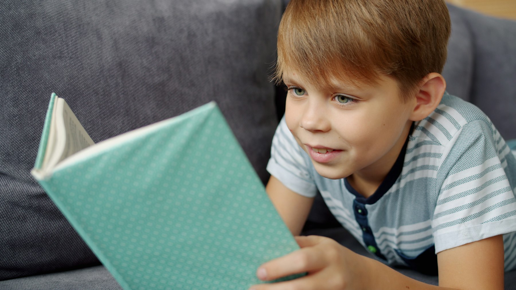 Menino lendo um livro confortavelmente no sofa